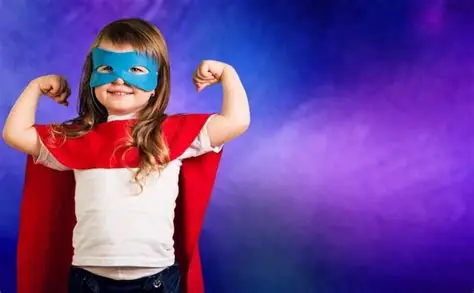 Una niña disfrazada de superheroína, con capa y antifaz, saca músculo sonriendo